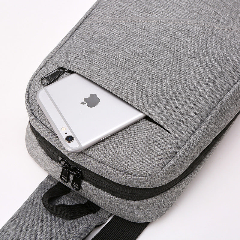 A grey sling bag is shown from a top-down angle, with a silver iPhone placed in its open top pocket.